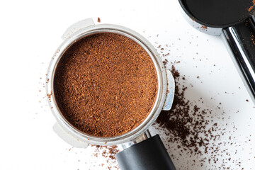 A metal coffee portafilter, measuring spoon, and loose coffee grounds lie on a white background