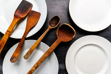 Big white plates and old wooden utensils on black chalkboard background. Flat lay. Top view. Food concept. Dark mood food photography.