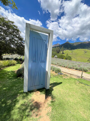 Surreal blue door frame standing open in sunny green field with mountains and blue sky background