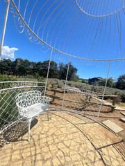 White decorative chair inside a large, spiraling white metal garden structure on a sunny day