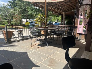 Outdoor patio seating area of a restaurant or cafe with tables, chairs, and a large umbrella providing shade on a sunny day