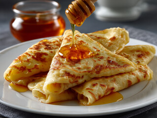 Golden crepes on white plate drizzling with honey