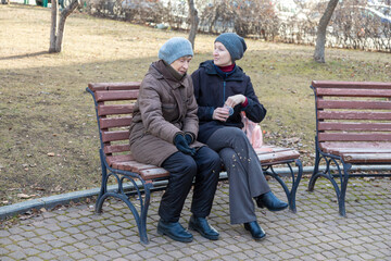 Two women sitting on park bench having a warm conversation. Intergenerational bond, social care and...