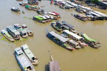 Obraz premium Aerial perspective reveals a lively cluster of covered market boats trading produce on the river at Cai Rang floating market in Can Tho, Mekong Delta, Vietnam. The scene features colorful tarps