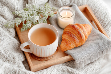 Breakfast tray with tea, croissant, and candle on a cozy blanket in a light-filled morning setting
