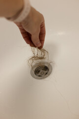 Woman takes loss hair out of water drain hole of a shower. Closeup.