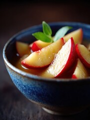 Fresh apple slices arranged in a blue bowl with mint leaves on a textured dark background