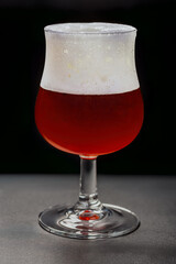 Unique lambic beer served in a glass at a brewery in Belgium featuring a rich cherry color with foam on top