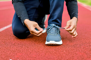 Runner tying shoelaces on red track, close-up on feet and hands, preparing for race or workout