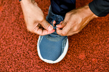 Close-up of person tying shoelaces on blue running shoe on red track