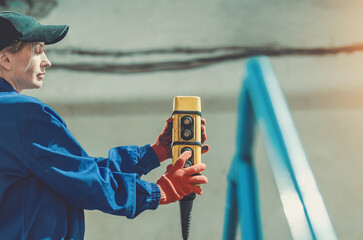 Female worker in protective gear and orange gloves working with control panel at production facility.