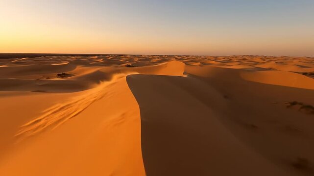 Wide aerial drone shot flying slowly over vast, empty yellow sand dunes where wind causes subtle surface deformation during golden hour light yellow sand dunes, dune waves, flying slowly