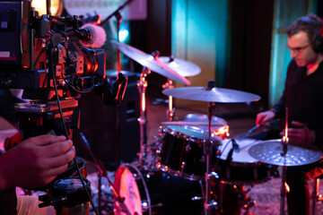 Naklejka premium Professional camera setup recording a drum set and musician performing live on stage, capturing music production for a concert, film, or documentary