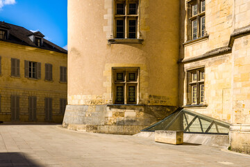 Warm afternoon sunlight highlights the textured stone walls and classic mullioned windows of a historic building in Nevers. The scene features geometric shadows, pale masonry, and a modern glass
