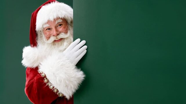 Santa in traditional red costume hides playfully behind green panel with gloved hand visible suggesting secret christmas message surprise discount or warm holiday invitation