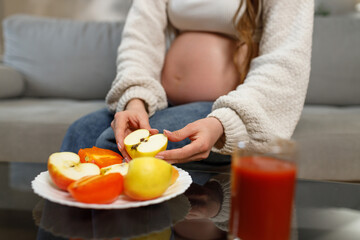 Pregnant woman holding apple slices with persimmons and juice nearby, focusing on healthy nutrition during pregnancy