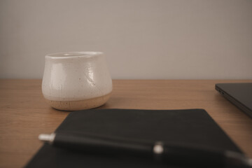 A black notebook lies open with a pen resting on top, accompanied by a white coffee cup filled with dark coffee. This setup invites creativity and reflection