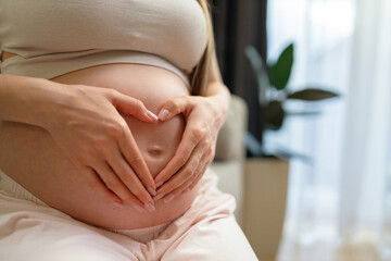 Woman's hands form heart shape on pregnant belly, symbolizing love and anticipation for new life