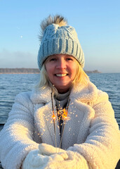 happy smiling woman with sparklers at the frozen sea