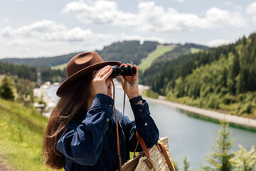 A woman stands by a river wearing a hat