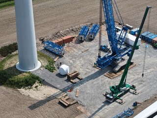 Lattice boom crawler crane awaits the assembly of a new wind turbine in the wind farm, aerial view, preparation, construction site, energy transition
