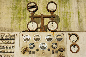 A wall with a bunch of dials and gauges on it. The gauges are old and rusted