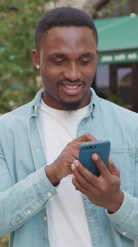 Portrait of man with small beard and in earrings which previsioning phone programs on the background of cozy outdoors cafe,4k