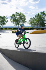 Obraz premium Child cyclist practicing in skate park during summer sunny day