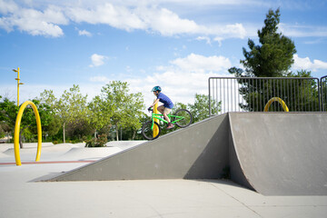 Young boy riding bike up ramp in skatepark on sunny day