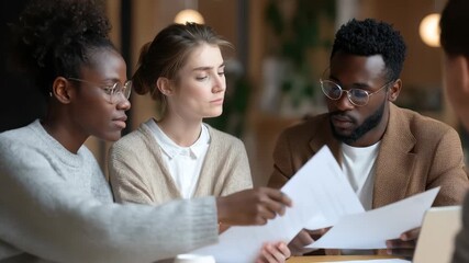 Multiracial coworkers collaborate on project analysis in cozy workspace while reviewing documents and exchanging ideas