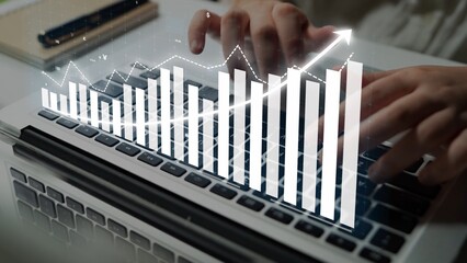 A close-up view of hands typing on a laptop keyboard with a digital overlay of a rising graph, symbolizing financial growth and data analysis in a professional setting. Copula