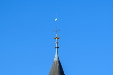 Close-up of a decorative metal spire with a weather vane atop a slate turret roof, set against a vivid clear blue sky at La Conciergerie in Paris. © Florent