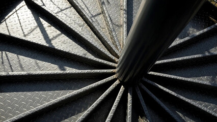 A unique top-down perspective captures the concentric rings and radial pattern of a sturdy metal spiral staircase bathed in sunlight.