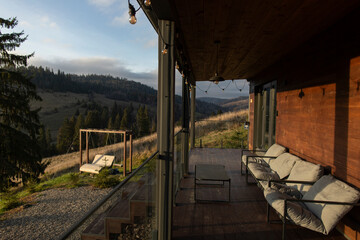 Terrace with seating area set up on wooden deck, scenery view with rolling mountains and trees, cozy atmosphere of relaxation on nature