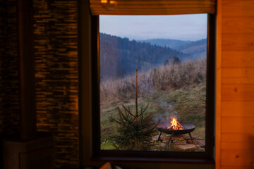 Fototapeta premium Fire pit outside cabin, view form window on mountains and backyard in the evening