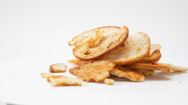 A loose pile of baked bread slices and crumbs rotates smoothly on a white background. The video highlights crunchy texture, irregular shapes, and golden browning through continuous rotation.