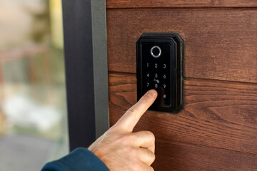 Male hand pressing button on keypad at entrance to unlock door mounted on wooden wall, keypad has numbers
