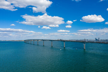 Obraz premium A long concrete bridge curves across turquoise water under a sky filled with scattered cumulus clouds, connecting the mainland to Ile de Re in Charente-Maritime, western France. The open seascape