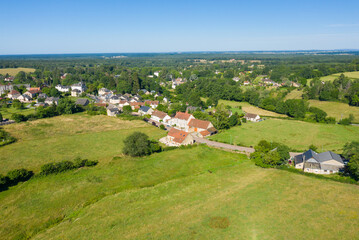 Obraz premium Aerial photo of Saint-Honore-les-Bains reveals a tranquil village nestled among lush green fields and surrounded by dense forest under a clear blue sky.