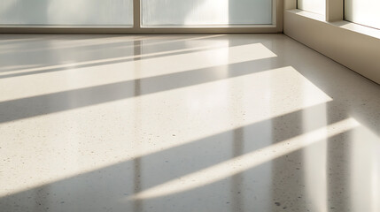 Sunlight streaming through a window casts sharp shadows across a modern, neutral-toned stone floor, creating a minimalist, serene space.