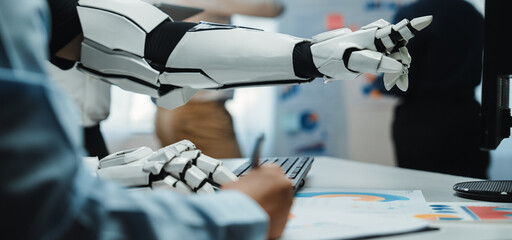 A robotic arm points at graphical reports while a human writes notes in a modern office, showcasing the synergy between advanced technology and human expertise in business settings.Noogenesis