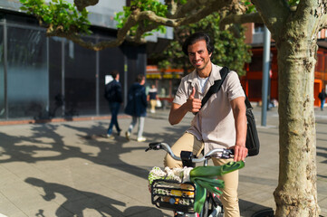 Indian business man standing with his bicycle and groceries on a city street, giving thumbs up. Promoting sustainable lifestyle