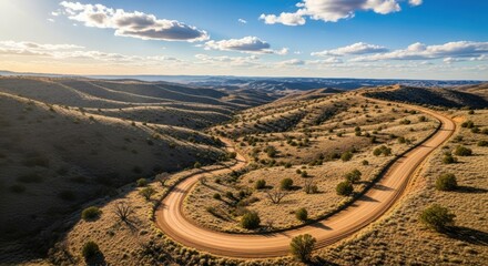 Winding Dirt Road Through Arid Hills Under a Blue Sky with Clouds.