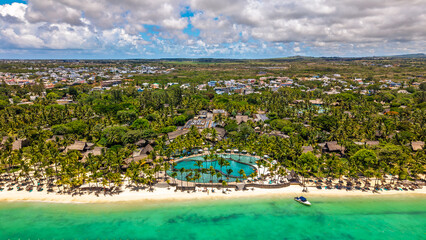 Aerial panoramic view of a luxury tropical beach resort with curved swimming pool and beachfront thatched roof bungalows