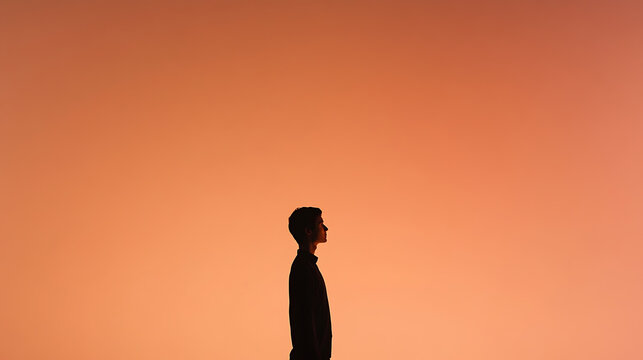 A solitary figure stands silhouetted against a warm, diffused coral backdrop. The minimalist composition evokes a sense of contemplation and introspection in the quiet space.