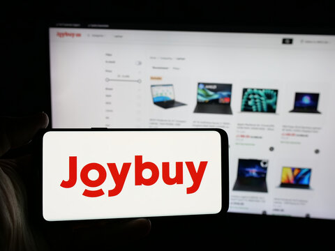 Stuttgart, Germany - 12-17-2025: Person holding smartphone with logo of e-commerce company Joybuy (Joybuy.com) on screen in front of website. Focus on phone display.