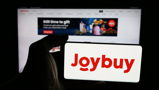 Stuttgart, Germany - 12-17-2025: Person holding mobile phone with logo of e-commerce company Joybuy (Joybuy.com) on screen in front of web page. Focus on phone display.