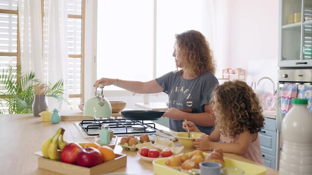 Joyful family moment with a mother and her daughter cooking breakfast in their modern kitchen. The woman is preparing to cook on the stove