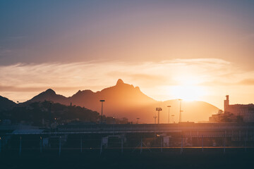 Telephoto view of sunrise over Rio de Janeiro mountains behind an airport runway and fence, warm golden haze and city silhouette, dramatic aviation travel background