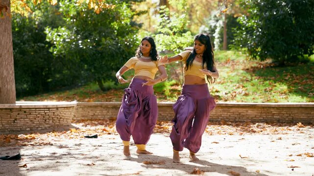 Young indian female dancers performing a traditional bollywood choreography. Graceful artists moving in sync with expressive gestures and movements outdoors